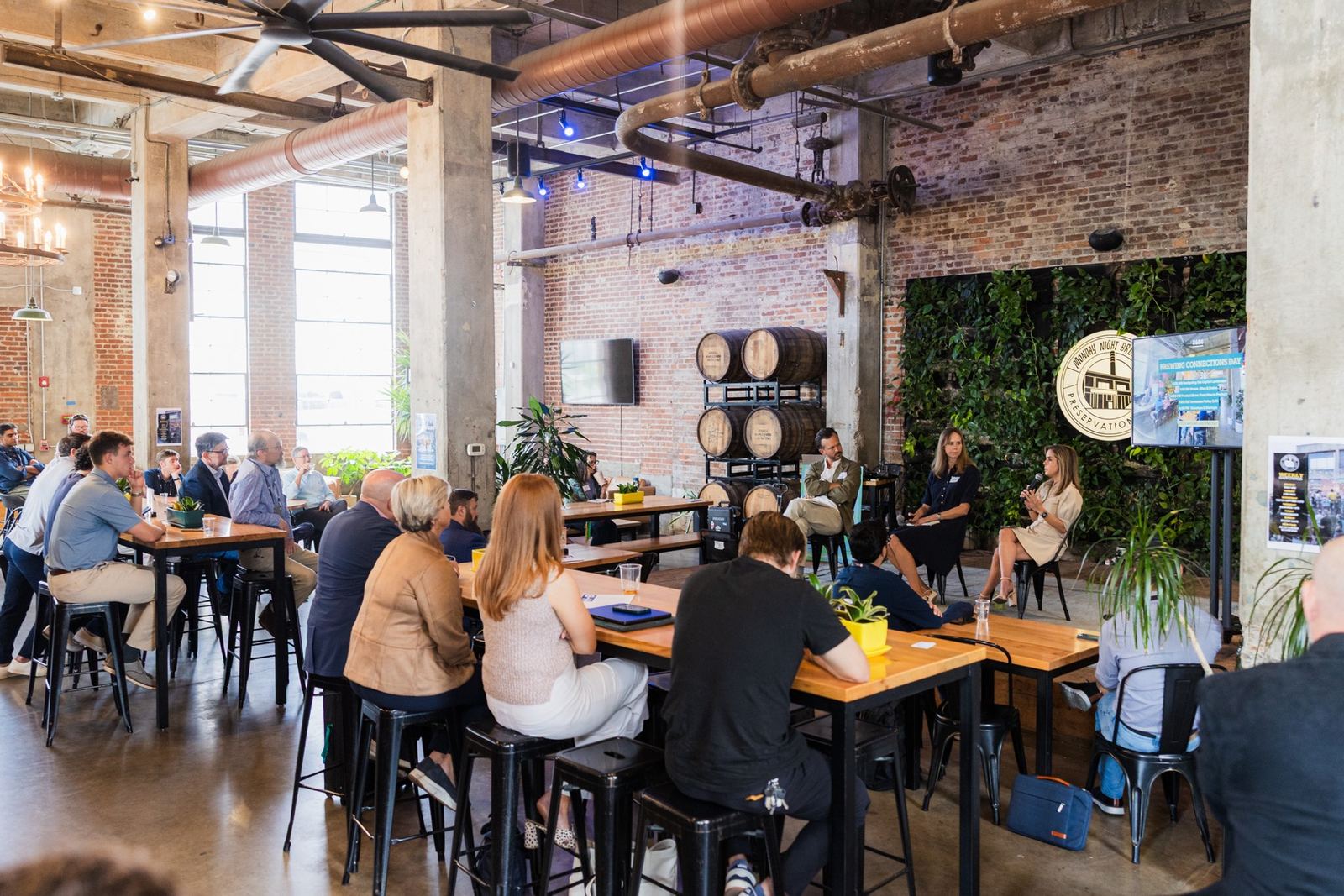 Founders and investors at long wooden tables listening to a panel in the brick and copper room at Monday Night Brewing during Brewing Connections Day 2025.